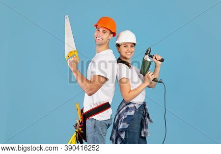 Repair Team. Happy Couple In Hard Hats Posing With Hand Saw And Drill Over Blue Background In Studio