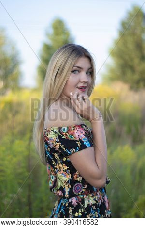 Overlight Bright Portrait Of A Charming Attractive Blonde In Flowery Dress In The Field