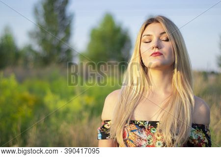 Overlight Bright Portrait Of A Charming Attractive Blonde In Flowery Dress In The Field