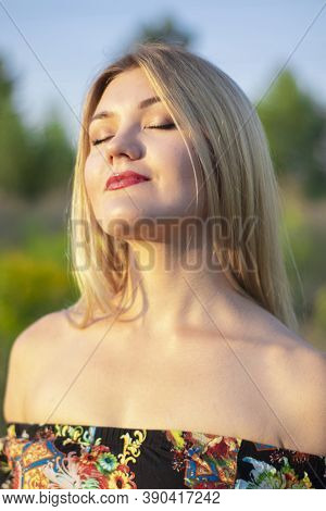 Overlight Bright Portrait Of A Charming Attractive Blonde In Flowery Dress In The Field