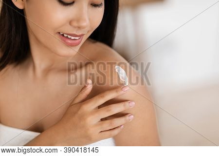 Body Care Concept. Closeup Of Asian Woman Wrapped In Towel Using Body Nourishing Cream Or Lotion. Un