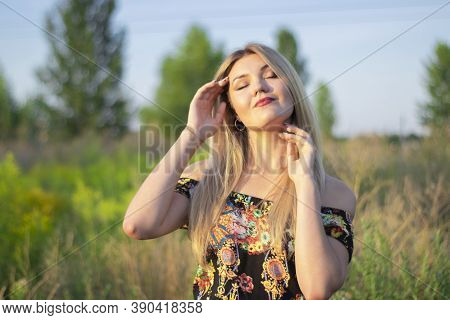 Overlight Bright Portrait Of A Charming Attractive Blonde In Flowery Dress In The Field