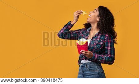 Tasty Fast Food. Portrait Of Hungry Black Fit Female Model Eating Delicious French Fries, Posing Wit