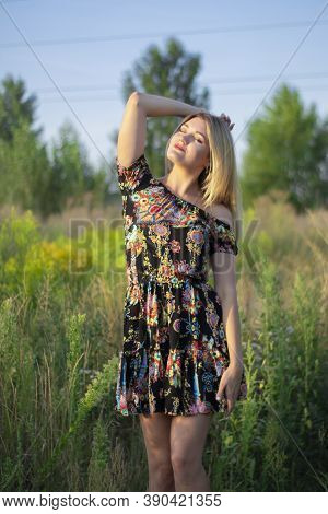 Overlight Bright Portrait Of A Charming Attractive Blonde In Flowery Dress In The Field