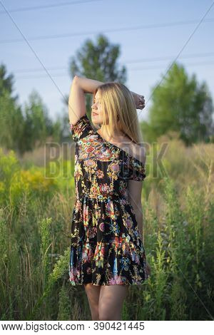 Overlight Bright Portrait Of A Charming Attractive Blonde In Flowery Dress In The Field