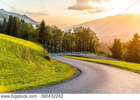 Romantic Sunset In The Mountains. Alpine Rural Curvy Road, Green Meadows And High Peaks Of Austrian 