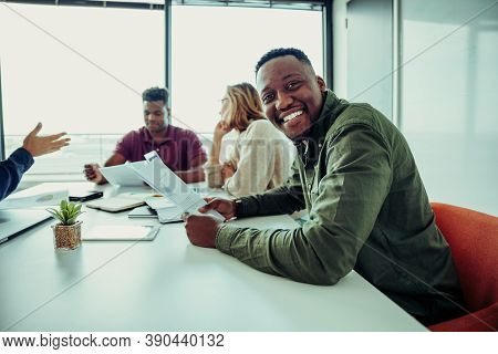 Mixed Race Business Man Smiling Working Through Paperwork With Parters Sitting Around Table In Confe