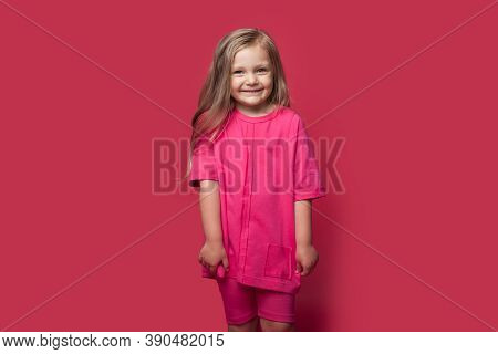 Monochrome Photo Of A Caucasian Small Blonde Girl Smiling At Camera In Casual Clothes On A Red Studi