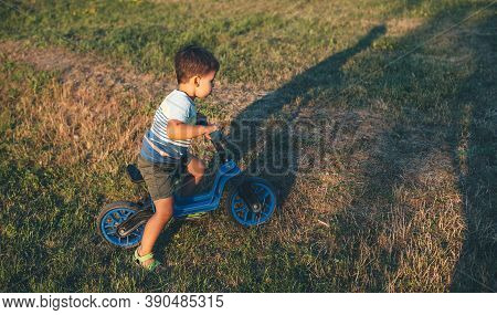 Young Caucasian Boy Riding A Bike On A Green Field Is Having Joy In A Summer Sunny Evening