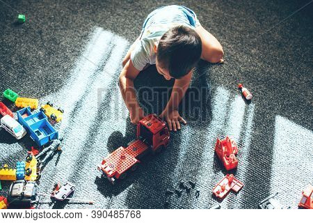 Upper View Photo Of A Caucasian Boy Playing With Constructor Car While Sitting On The Floor And Prac