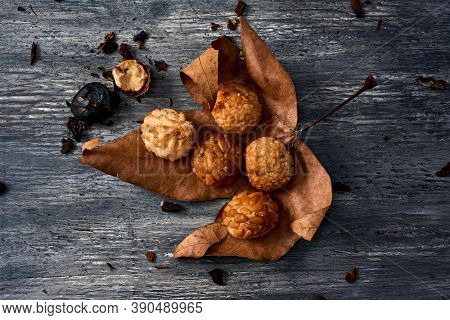 high angle view of some different panellets, typical confection of Catalonia, Spain, eaten traditionally in All Saints Day, on a dry leaf placed a rustic gray wooden table next to a roasted chestnut