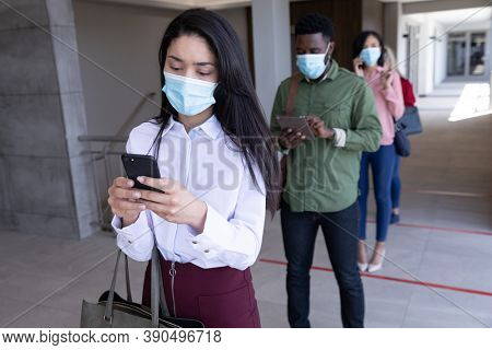 Multi ethnic group of male and female coworkers wearing face masks waiting for health check before entering office. Hygiene and social distancing in workplace during Coronavirus Covid 19 pandemic.