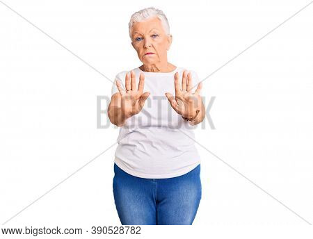 Senior beautiful woman with blue eyes and grey hair wearing casual white tshirt moving away hands palms showing refusal and denial with afraid and disgusting expression. stop and forbidden. 