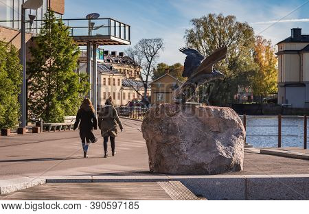 Two Women Pass A Beautiful Eagle Statue At The Munktellbadet  On A Beautiful Autumn Day In Eskiltuna