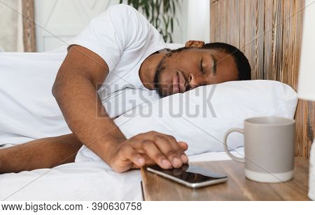 Oversleeping. Asleep African Man Sleeping Through Alarm Clock On Smartphone Waking Up In The Morning