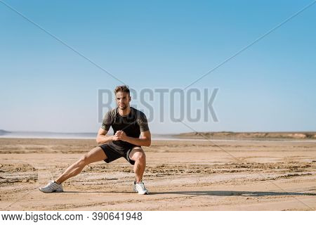 Motivated focused young sportsman exercising at the beach, stetching