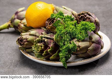 Fresh French Petit Violet Artichokes Heads Cultivted In Brittany, France With Lemon And Parsley