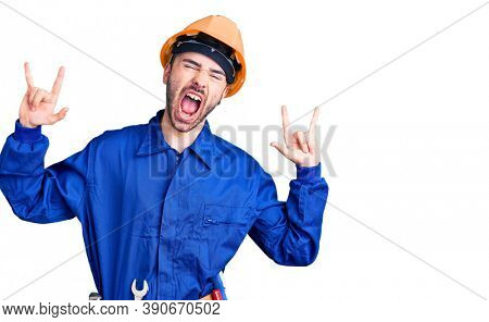 Young hispanic man wearing worker uniform shouting with crazy expression doing rock symbol with hands up. music star. heavy music concept. 