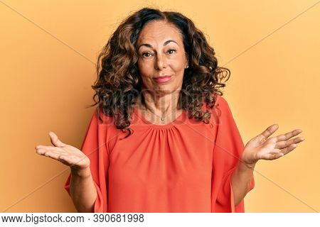 Middle age hispanic woman wearing casual clothes clueless and confused expression with arms and hands raised. doubt concept. 