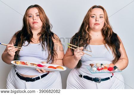 Plus size caucasian sisters woman eating sushi using chopsticks relaxed with serious expression on face. simple and natural looking at the camera. 