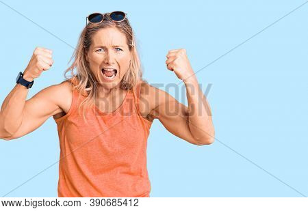 Middle age fit blonde woman wearing casual summer clothes and sunglasses angry and mad raising fists frustrated and furious while shouting with anger. rage and aggressive concept. 