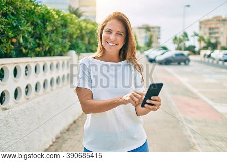 Beautiful middle age hispanic woman smiling using smatphone happy outdoors