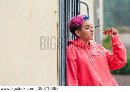 Portrait Of A Young Girl With Short Colorful Hair And Nose Piercing Satanding Near The Wall With Woo