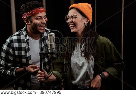Portrait Of Cheerful Young Man And Woman, Duet Singing Into A Condenser Microphone While Recording A