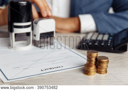Businessman Approves Important Contract. Stack Of Coins, Contract And Stamps On Desk Close-up. Busin