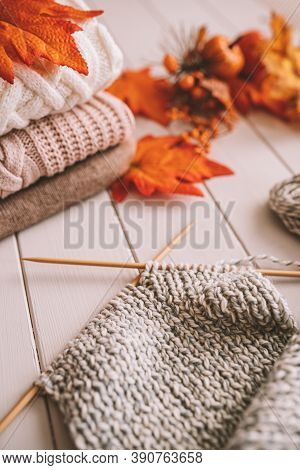 A Stack Of Knitted Sweaters Close Up With Knitting Scarf And Autumn Decarations On A White Wooden Ba