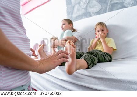 Mom Tickles Her Sons Bare Heels. The Boy Is Sitting On The Sofa And Laughing Merrily.