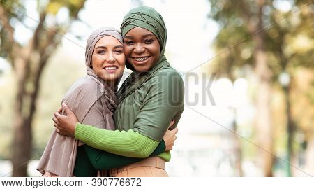 Two Muslim Ladies In Hijab Hugging Smiling To Camera Posing Standing In Park Outdoors. Female Friend