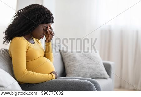 Young Pregnant Black Woman Suffering From Headache Or Migraine, Feeling Sick, Sitting On Sofa At Hom