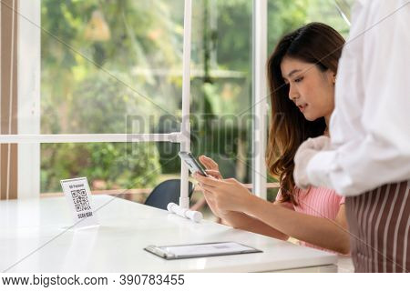 Asian woman customer use mobile phone scan qr code to make online contactless mobile payment after eating out in new normal social distance restaurant. Online contactless and technology concept.