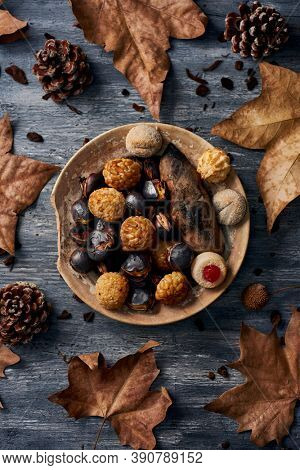 high angle view of a plate with some roasted sweet potato, some roasted chestnuts and some panellets, typical confection of Catalonia, Spain, eaten traditionally in All Saints Day, on a rustic table