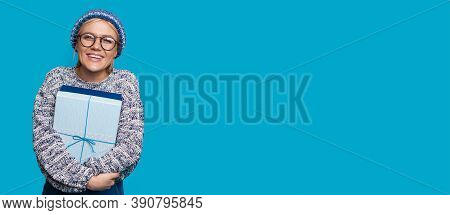 Cute Woman With Hat And Blonde Hair Is Embracing A Present On A Blue Wall With Free Space While Adve