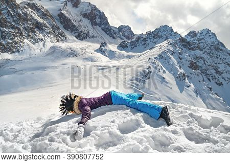 Acrophobia Woman In Funny Mohawk Hat Lie On Top Of A Snowy Rock Cliff Edge. Fighting The Fear Of Hei