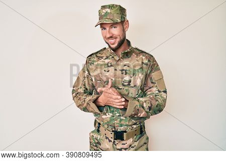 Young caucasian man wearing camouflage army uniform with hands together and crossed fingers smiling relaxed and cheerful. success and optimistic 