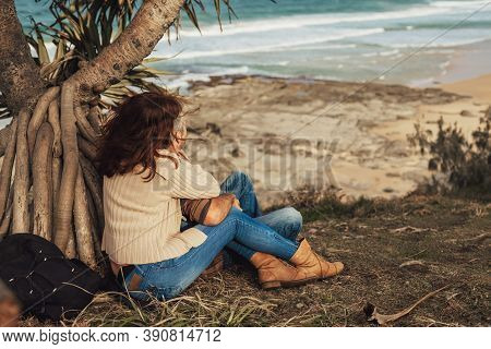 Happy Middle-aged Couple In Love Sitting Under The Tree With Ocen View, Hug, Smile And Look At The O