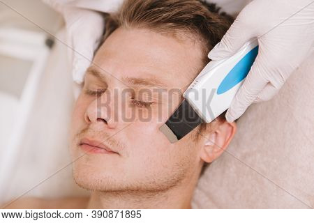 Handsome Young Man Receiving Facial Skin Cleanse By Professional Beautician Using Ultrasound Cleansi