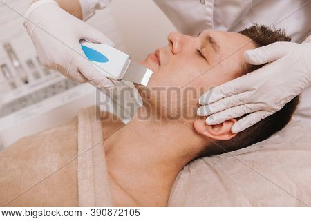 Unrecognizable Cosmetologist Using Ultrasound Skincare Device, Cleaning Skin Of A Male Client