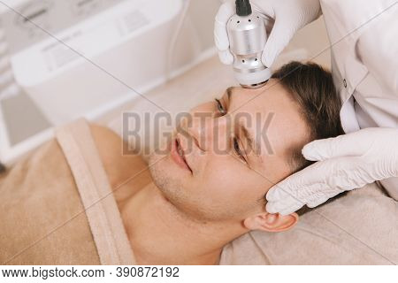 Professional Cosmetologist Using Rf-lifting Device On The Face Of Handsome Young Male Client