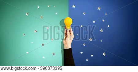 Person Holding A Yellow Light Bulb With Silver Shiny Stars