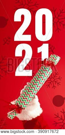 Hand Of Santa Claus Holding Gift, Greeting With New Year 2021 And Christmas. Red Background With Let