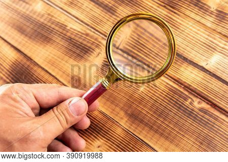Close-up Of A Magnifier In Hand On A Wooden Background.