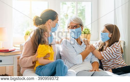 A nice girls, her mother and grandmother enjoying spending time together at home. People wearing face masks.