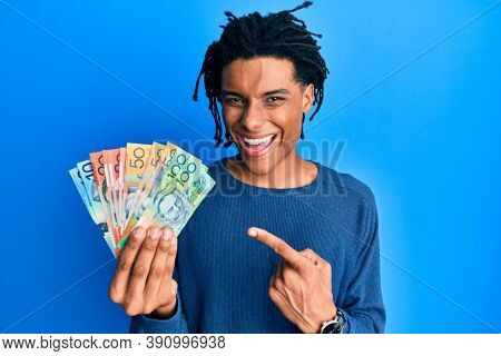 Young african american man holding australian dollars smiling happy pointing with hand and finger 