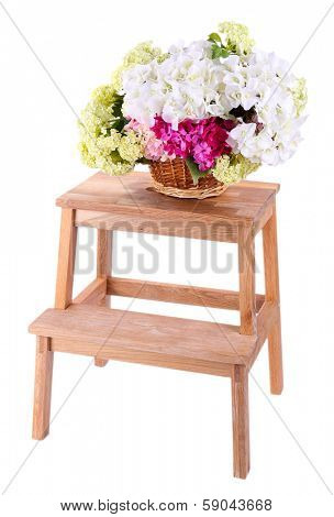 Wicker basket with flowers on small wooden ladder, isolated on white