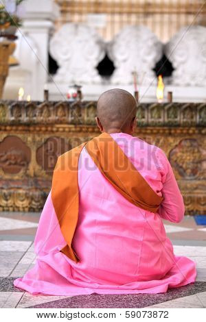 YANGON, MYANMAR - DECEMBER 4, 2013: Buddhist nun praying at the Shwedagon Paya - one of the most important pilgrimage destination for Theravada Buddhists.