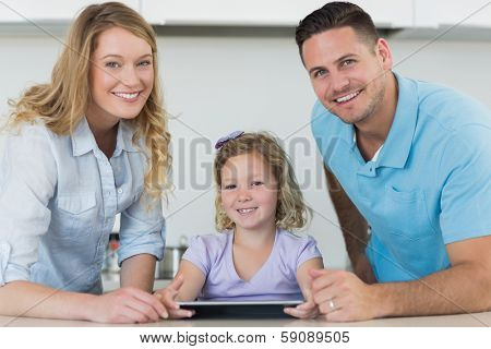Portrait of happy parents assisting cute girl in using digital tablet at table in kitchen